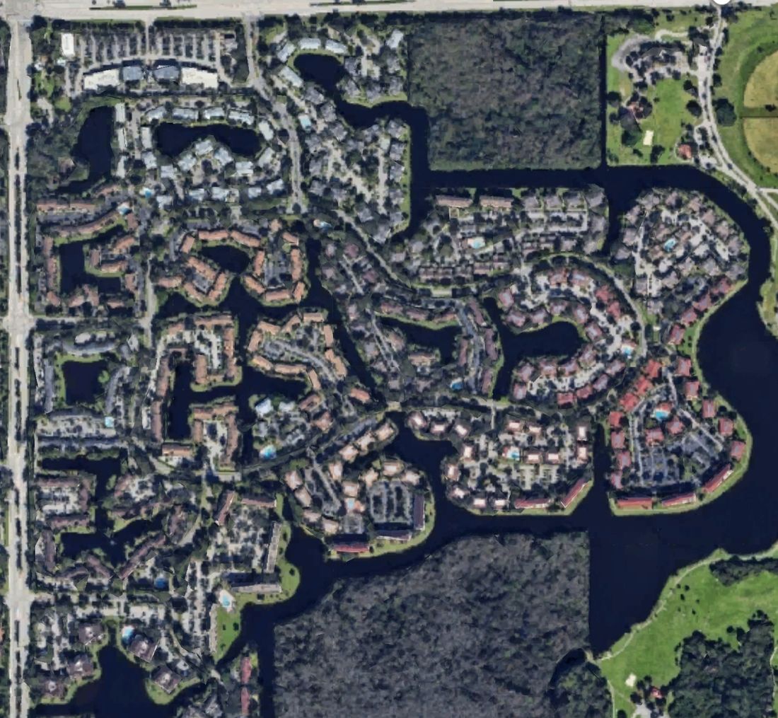 Aerial view of a lakeside condo and townhome community with shared roofs, pool decks and walkways